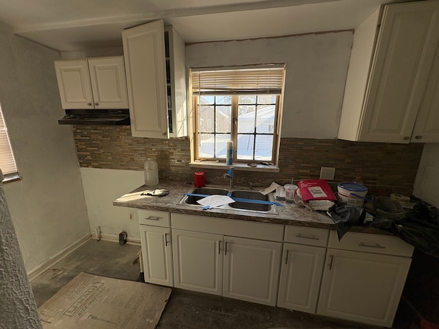 kitchen featuring dark countertops, backsplash, white cabinets, a sink, and baseboards