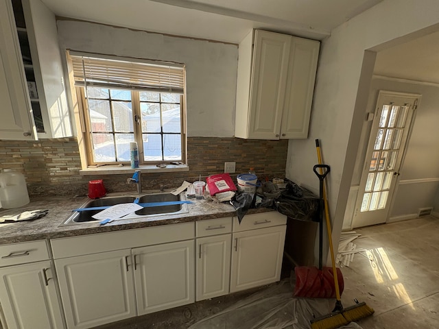 kitchen featuring tasteful backsplash, dark countertops, visible vents, white cabinets, and a sink