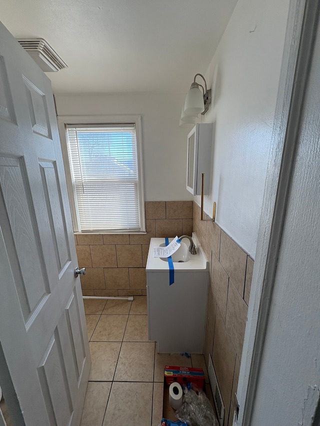 bathroom featuring tile walls, visible vents, wainscoting, a sink, and tile patterned floors