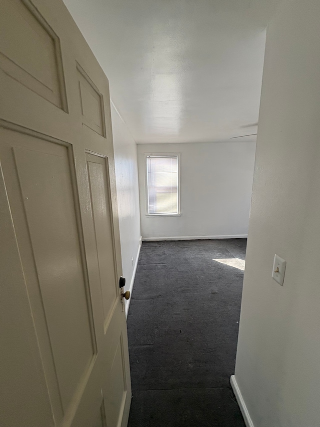 hall featuring dark carpet and baseboards