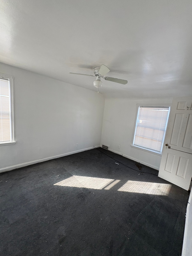 unfurnished room featuring dark colored carpet, a ceiling fan, visible vents, and baseboards