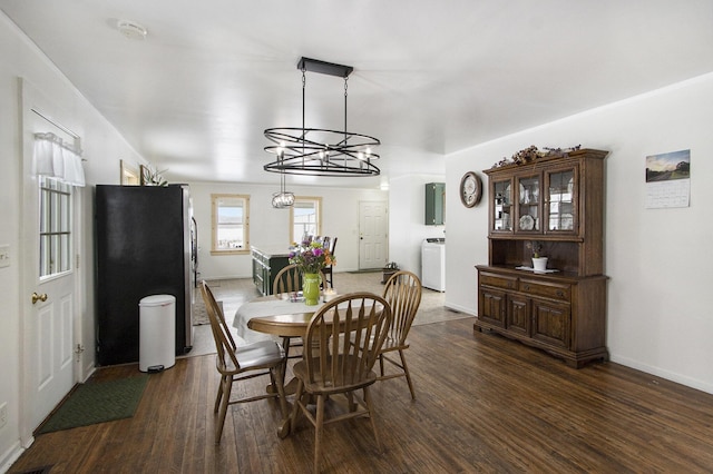 dining space with dark wood-style floors, washer / clothes dryer, a notable chandelier, and baseboards