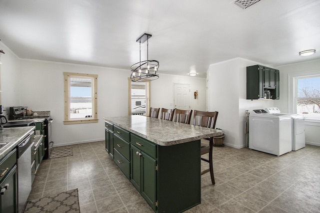 kitchen featuring stainless steel appliances, a kitchen island, washer and dryer, hanging light fixtures, and a kitchen bar