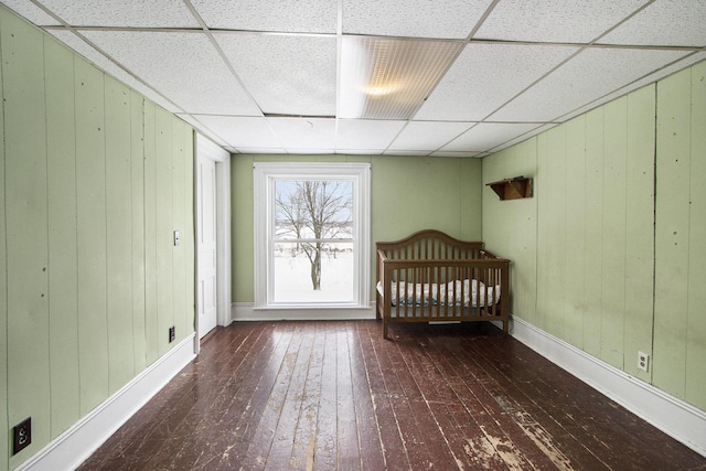 unfurnished bedroom with dark wood-type flooring, a paneled ceiling, wood walls, and baseboards