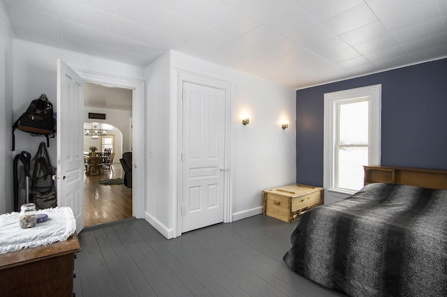 bedroom with arched walkways, dark wood finished floors, and baseboards