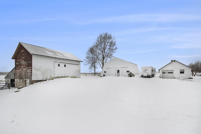 snowy yard featuring a detached garage and an outbuilding