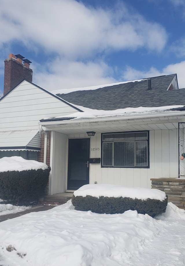 snow covered property entrance with covered porch and roof with shingles