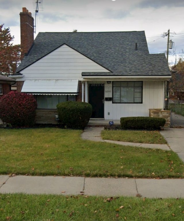 view of front facade with a chimney, roof with shingles, and a front yard