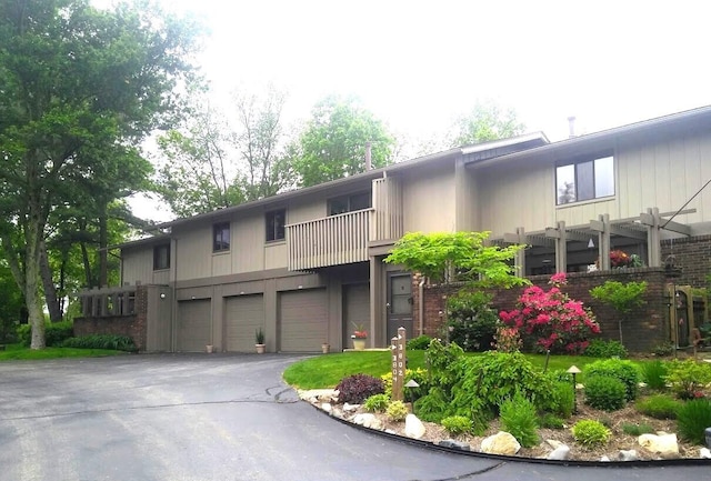 view of property featuring an attached garage, a balcony, brick siding, driveway, and a pergola