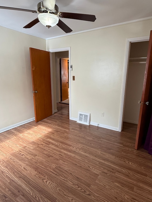 unfurnished bedroom with wood finished floors, visible vents, baseboards, ornamental molding, and a closet