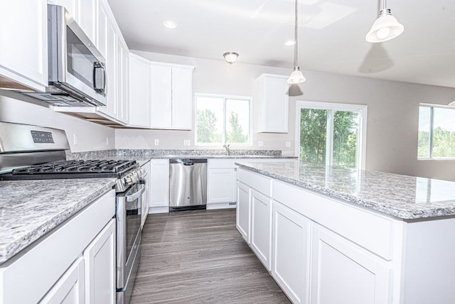 kitchen featuring decorative light fixtures, appliances with stainless steel finishes, white cabinetry, a kitchen island, and light stone countertops