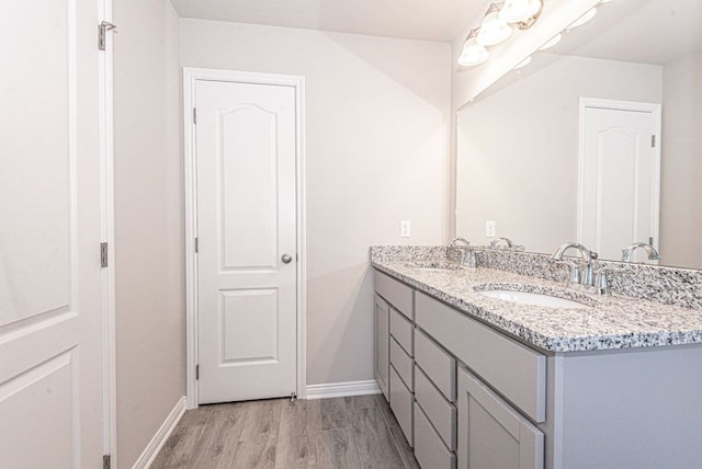 bathroom with double vanity, baseboards, a sink, and wood finished floors