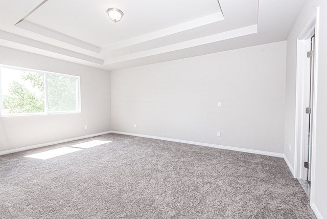 carpeted spare room featuring a tray ceiling and baseboards