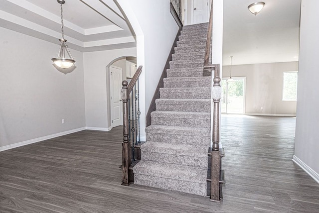 stairway featuring arched walkways, a tray ceiling, baseboards, and wood finished floors