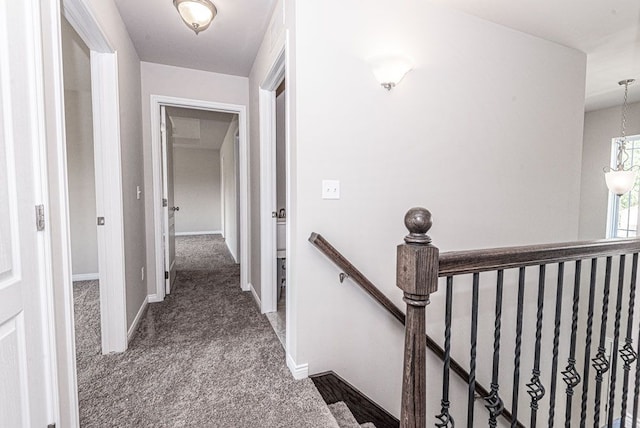 hallway with dark colored carpet, baseboards, and an upstairs landing