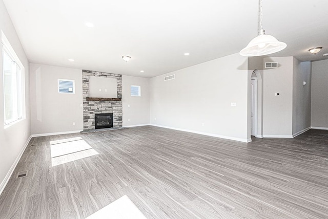 unfurnished living room featuring visible vents, wood finished floors, and a stone fireplace