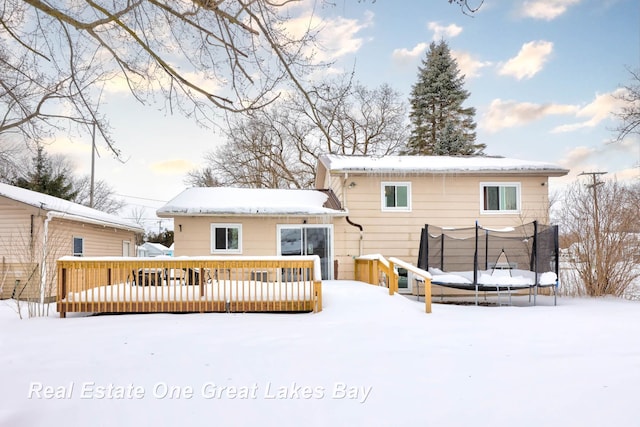 snow covered house featuring a trampoline and a deck