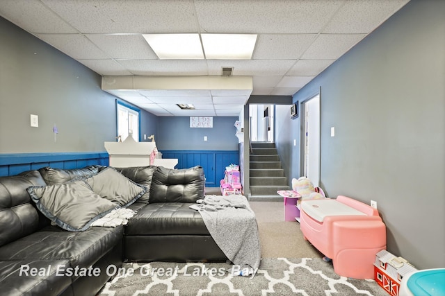 carpeted living area with stairs, visible vents, a drop ceiling, and wainscoting