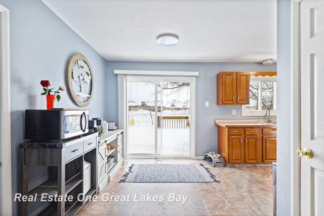 kitchen featuring light countertops, stainless steel microwave, a sink, and brown cabinets