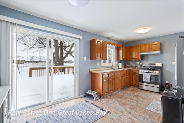 kitchen featuring light countertops, brown cabinetry, gas stove, a sink, and under cabinet range hood