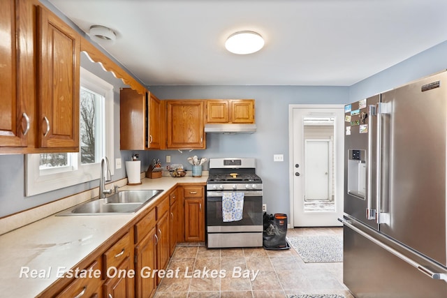 kitchen featuring under cabinet range hood, stainless steel appliances, a sink, light countertops, and brown cabinetry