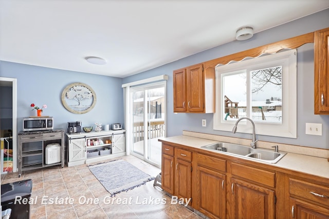 kitchen with brown cabinets, light countertops, stainless steel microwave, and a sink