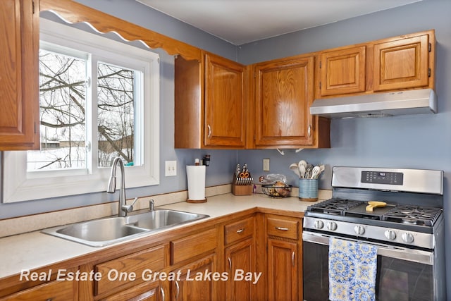 kitchen featuring stainless steel gas range oven, under cabinet range hood, a sink, light countertops, and brown cabinetry