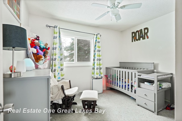 bedroom featuring a textured ceiling, ceiling fan, a crib, and speckled floor