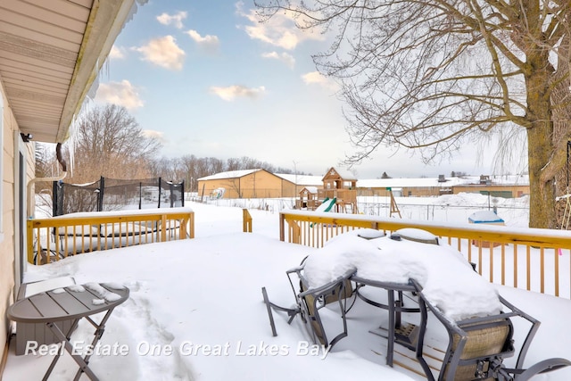 snow covered deck featuring a trampoline, a playground, and a fenced backyard