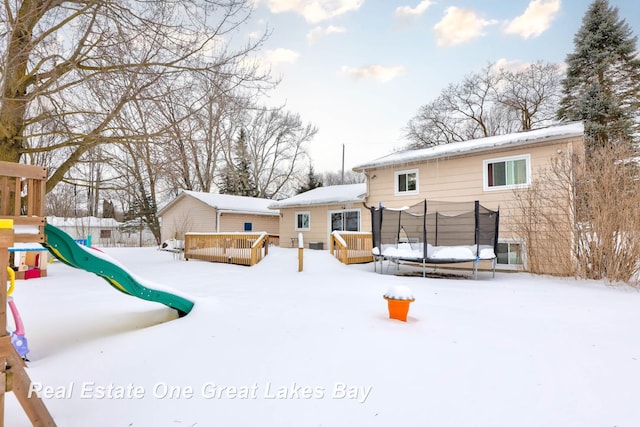 snow covered house with a trampoline, a playground, and a deck