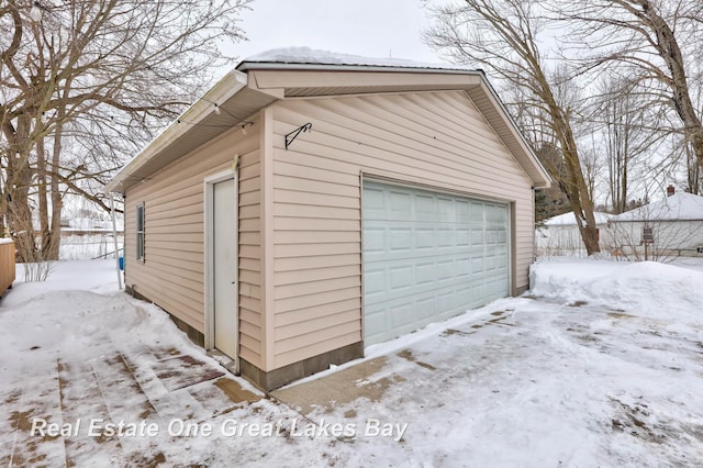 snow covered garage featuring a garage and fence