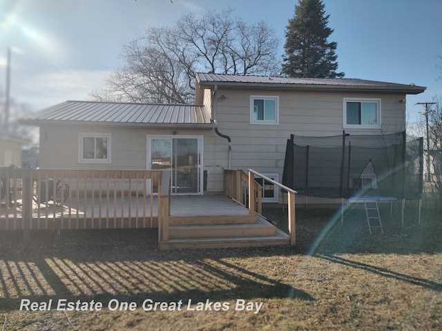 rear view of property with a trampoline, metal roof, and a wooden deck