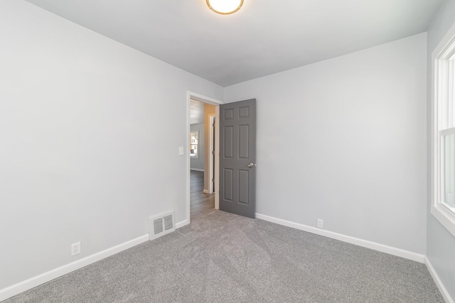 spare room featuring light carpet, a healthy amount of sunlight, baseboards, and visible vents