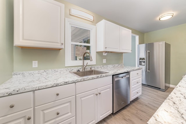 kitchen featuring light stone counters, a sink, white cabinetry, appliances with stainless steel finishes, and light wood finished floors