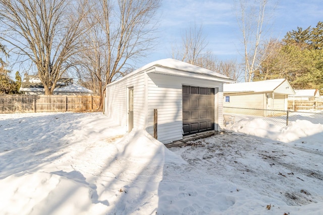 snow covered structure with fence and an outbuilding