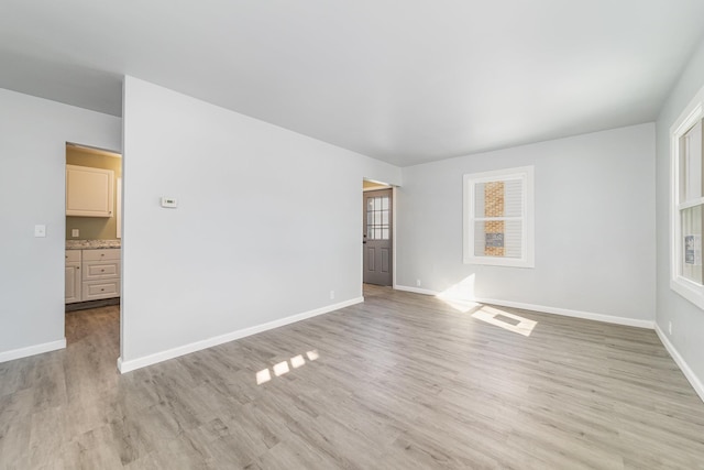 empty room with light wood finished floors, visible vents, and baseboards