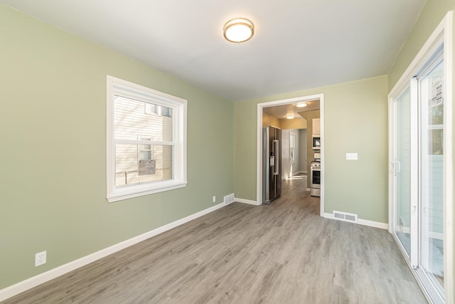 unfurnished room featuring light wood-style floors, visible vents, and baseboards