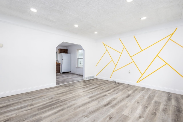 spare room with a textured ceiling, baseboards, and wood finished floors