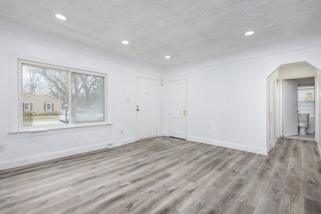 empty room with baseboards, visible vents, wood finished floors, a textured ceiling, and recessed lighting