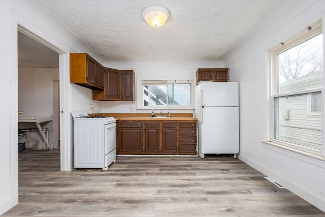 kitchen with a textured ceiling, light wood-type flooring, range with gas cooktop, and freestanding refrigerator