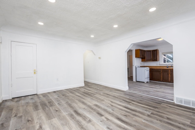 unfurnished living room with arched walkways, a textured ceiling, recessed lighting, visible vents, and light wood-type flooring