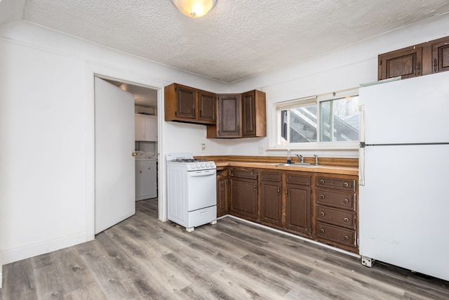 kitchen featuring a textured ceiling, white appliances, a sink, light countertops, and light wood finished floors