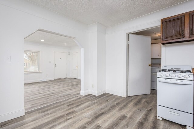 kitchen with dark brown cabinetry, light wood finished floors, arched walkways, a textured ceiling, and gas range gas stove