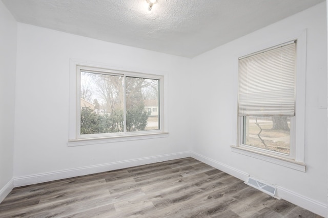 empty room with baseboards, a textured ceiling, visible vents, and wood finished floors