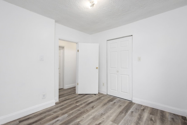 unfurnished bedroom featuring a closet, a textured ceiling, baseboards, and wood finished floors