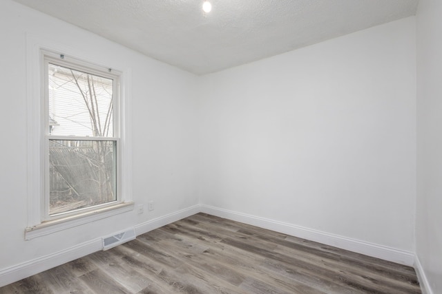 empty room with baseboards, a textured ceiling, visible vents, and wood finished floors