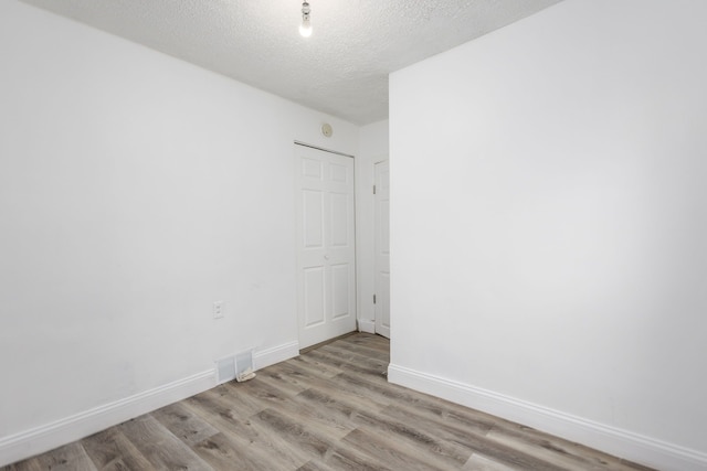 unfurnished room with baseboards, a textured ceiling, visible vents, and wood finished floors