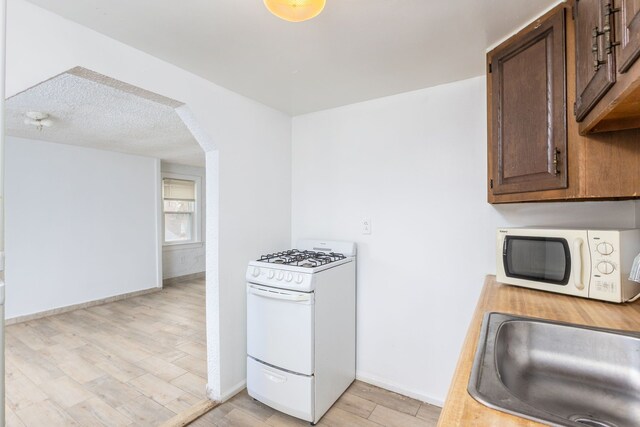 kitchen featuring arched walkways, white appliances, a sink, baseboards, and light wood-style floors