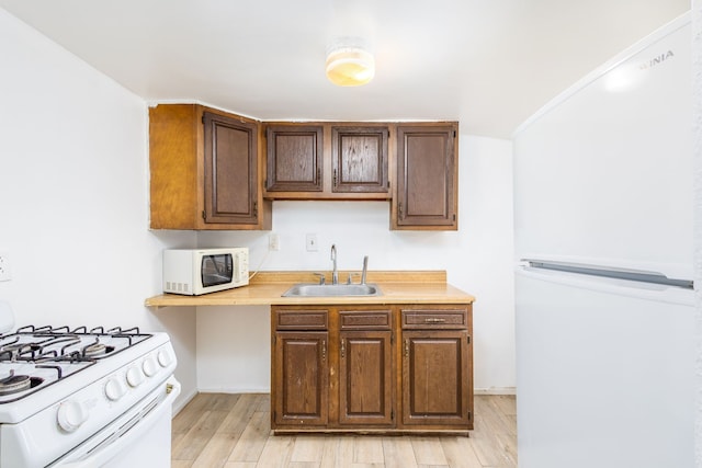 kitchen with white appliances, light wood finished floors, baseboards, light countertops, and a sink