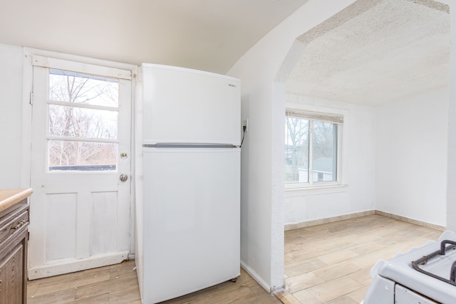 kitchen with white appliances, baseboards, arched walkways, light countertops, and light wood-style floors